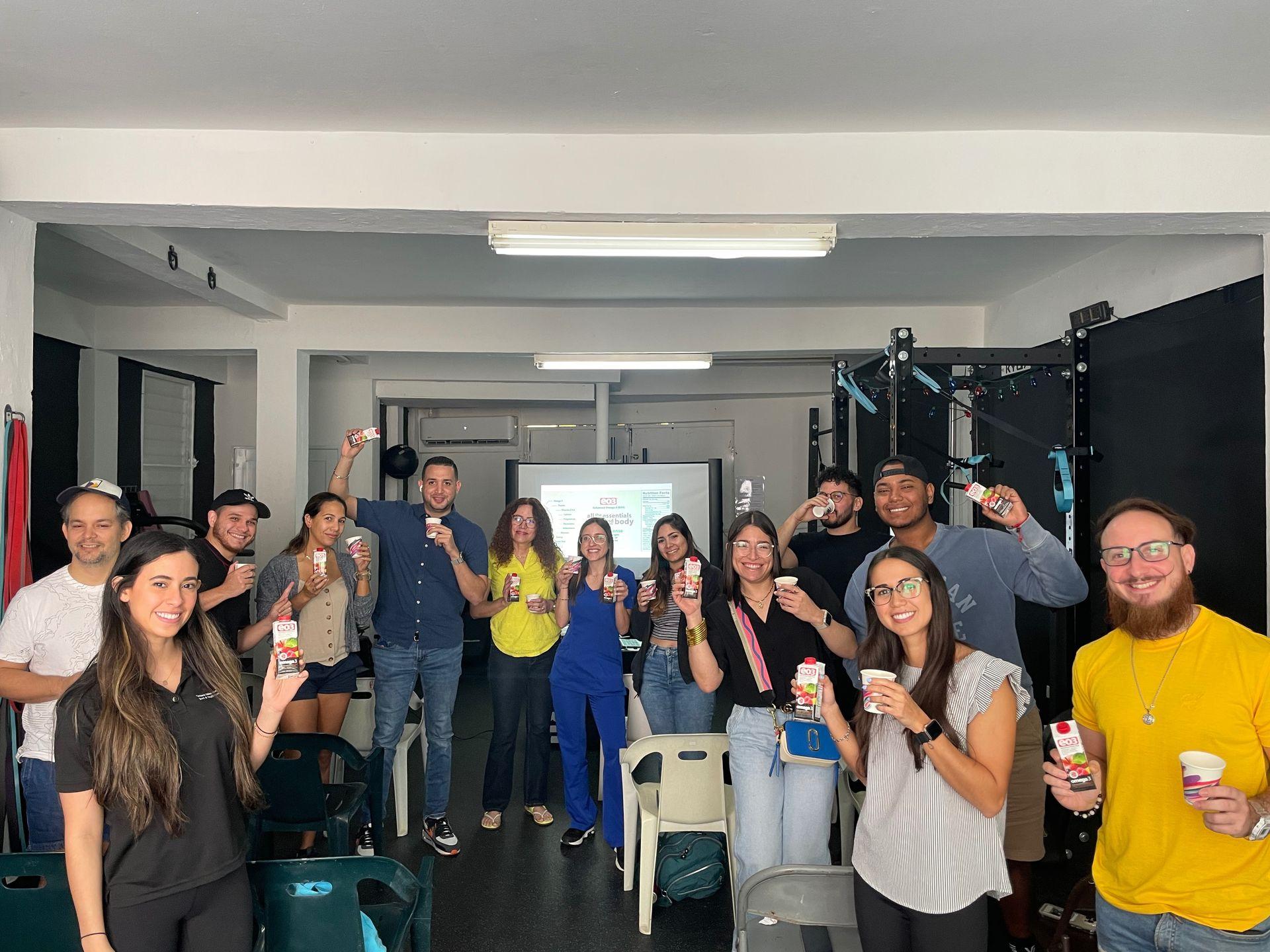 Group of people in a room holding up beverage cartons and smiling at the camera.